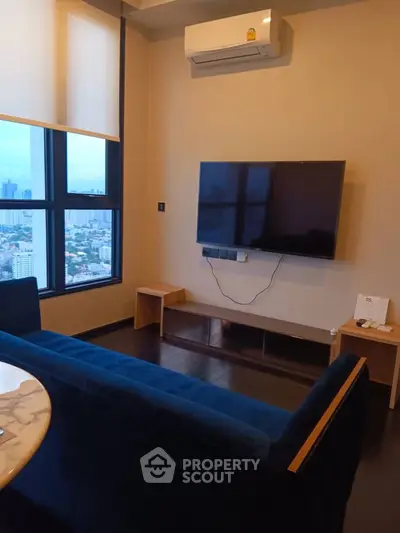 Modern living room with city view, featuring a wall-mounted TV and sleek furniture.