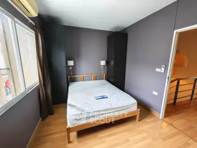 Cozy bedroom with wooden flooring and natural light, featuring a comfortable bed and modern decor.