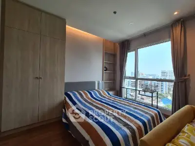 Cozy bedroom with large window offering city view and ample natural light.