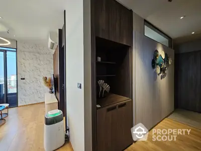 Modern apartment interior with stylish wood flooring, textured white brick wall, and contemporary furnishings, leading to a sunlit balcony.