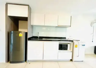 Modern kitchen with sleek cabinets, fridge, microwave, and washing machine in a bright space.