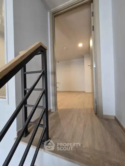 Modern interior with wooden flooring and open doorway, showcasing sleek railing design.