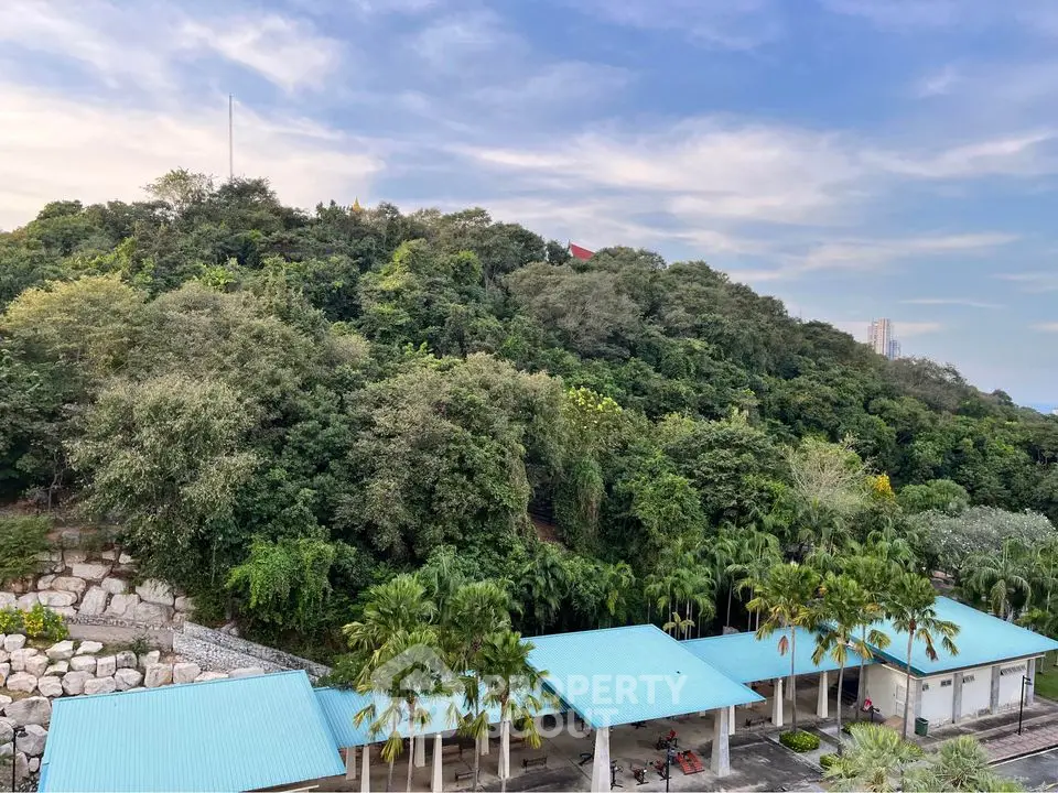 Scenic view of lush green hill with blue-roofed buildings in foreground, perfect for serene living.