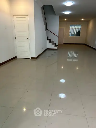 Spacious open-plan living area with glossy tiled floors and modern staircase.