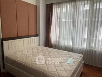Spacious bedroom with large windows and natural light, featuring a comfortable bed and elegant curtains.
