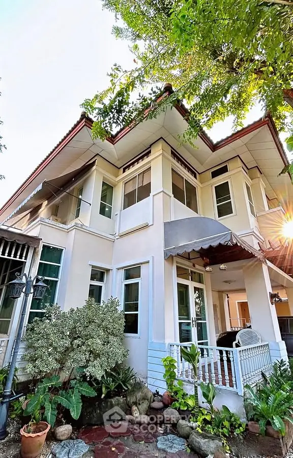 Charming two-story house with lush garden and inviting porch, perfect for family living.
