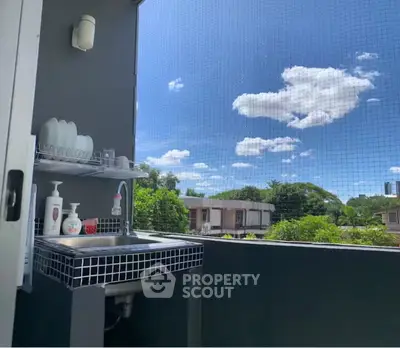 Charming balcony with outdoor sink and scenic view of lush greenery and blue sky.