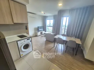 Modern open-plan living room with kitchen and dining area, featuring a washing machine and large windows.