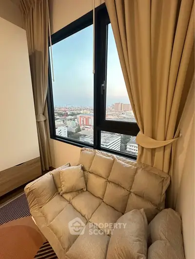 Cozy living room with plush sofa and panoramic city view through large window.