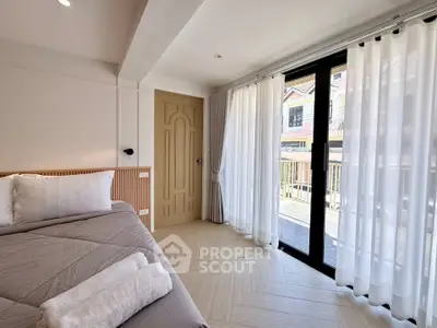Bright bedroom with large windows and balcony access, featuring modern decor and cozy bedding.