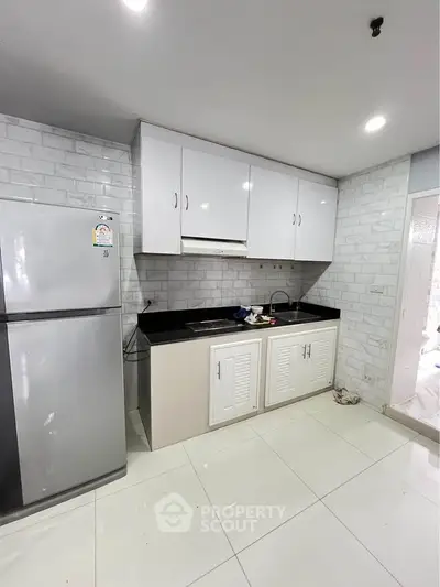 Modern kitchen with sleek white cabinets and stainless steel fridge in a stylish apartment.