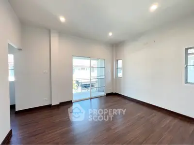 Spacious empty room with wooden flooring and large windows in modern home.