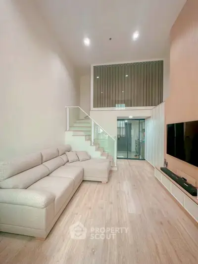 Spacious modern living room with high ceiling and elegant staircase in a stylish apartment.