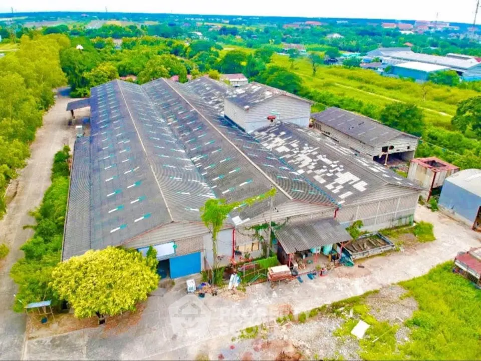 Expansive industrial warehouse with large roof and surrounding greenery, ideal for commercial use.