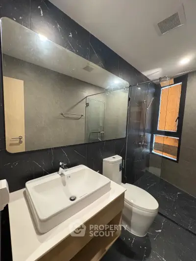 Modern bathroom with sleek black marble tiles and glass shower enclosure