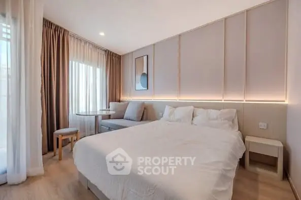 Modern bedroom with elegant decor and natural light, featuring a cozy seating area.