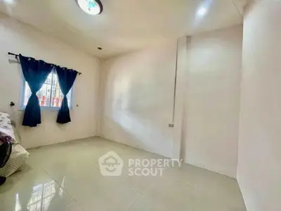 Spacious bedroom with natural light and tiled flooring, featuring a window with blue curtains.