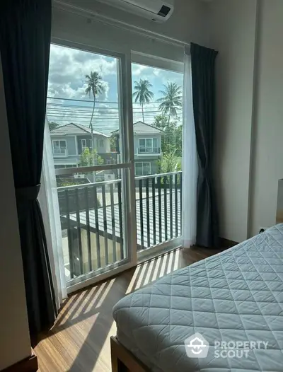 Bright bedroom with balcony view overlooking palm trees and houses