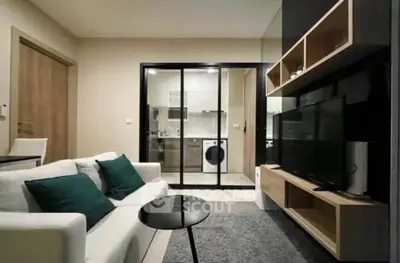 Modern living room with sleek furniture and view into stylish kitchen with washing machine.