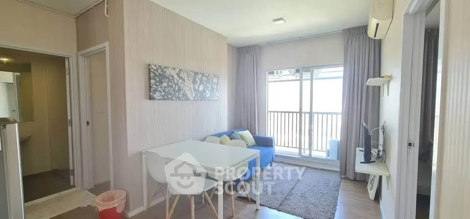 Modern living room with balcony, featuring a cozy blue sofa and sleek dining area.