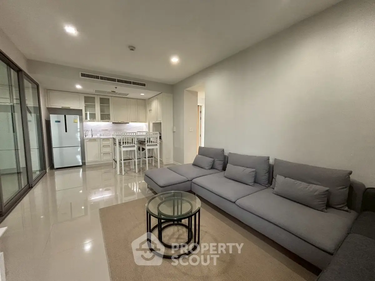 Modern living room with sleek kitchen, grey sofa, and glass coffee table in open layout.