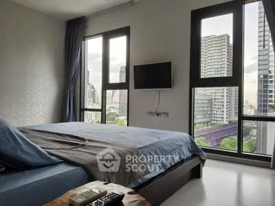 Modern bedroom with city view, featuring large windows and wall-mounted TV.