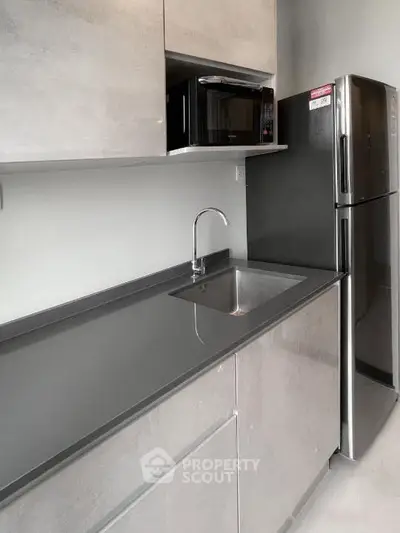 Modern kitchen with sleek countertops, stainless steel fridge, and built-in microwave.