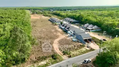Aerial view of a new residential development surrounded by lush greenery and open land.