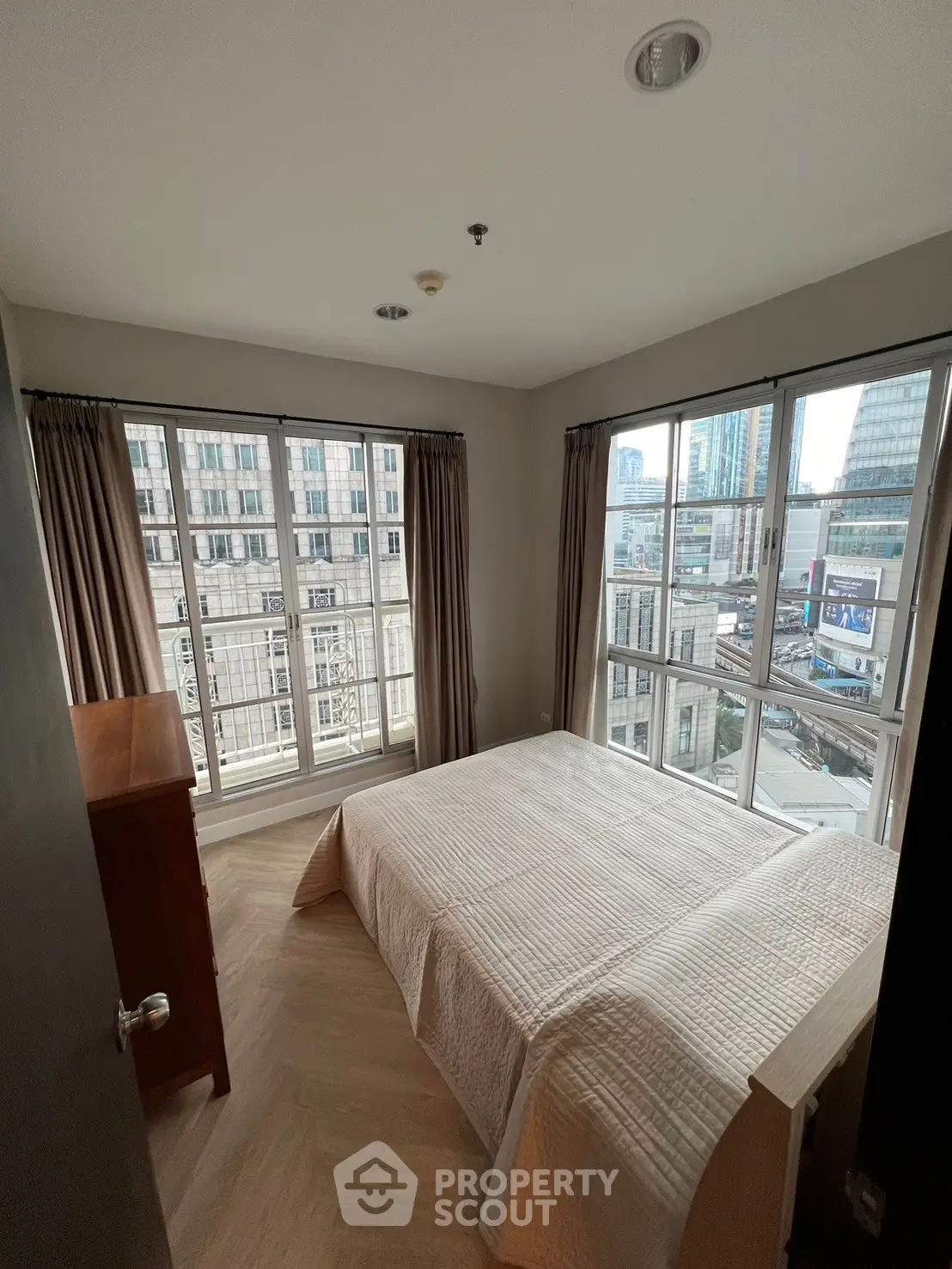 Spacious bedroom with large windows offering stunning city views in a modern apartment.
