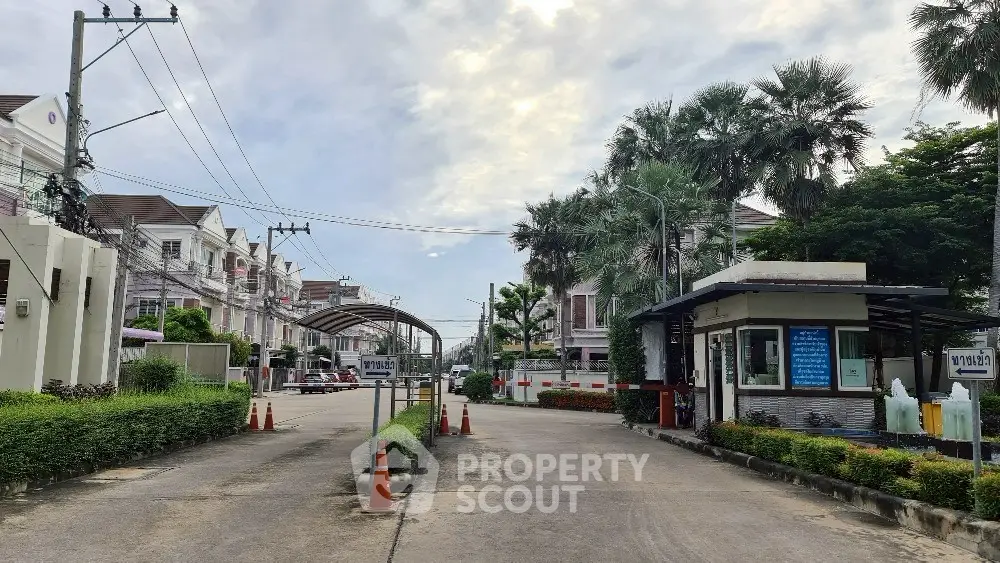 Charming residential community entrance with lush greenery and modern townhouses.