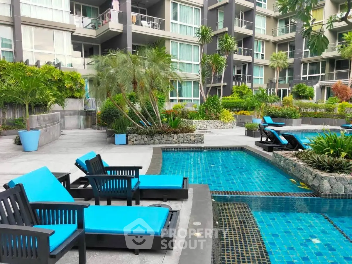 Luxurious apartment complex with poolside relaxation area and lush greenery.