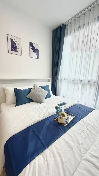 Modern bedroom with elegant decor, featuring a cozy bed with blue accents and large window for natural light.