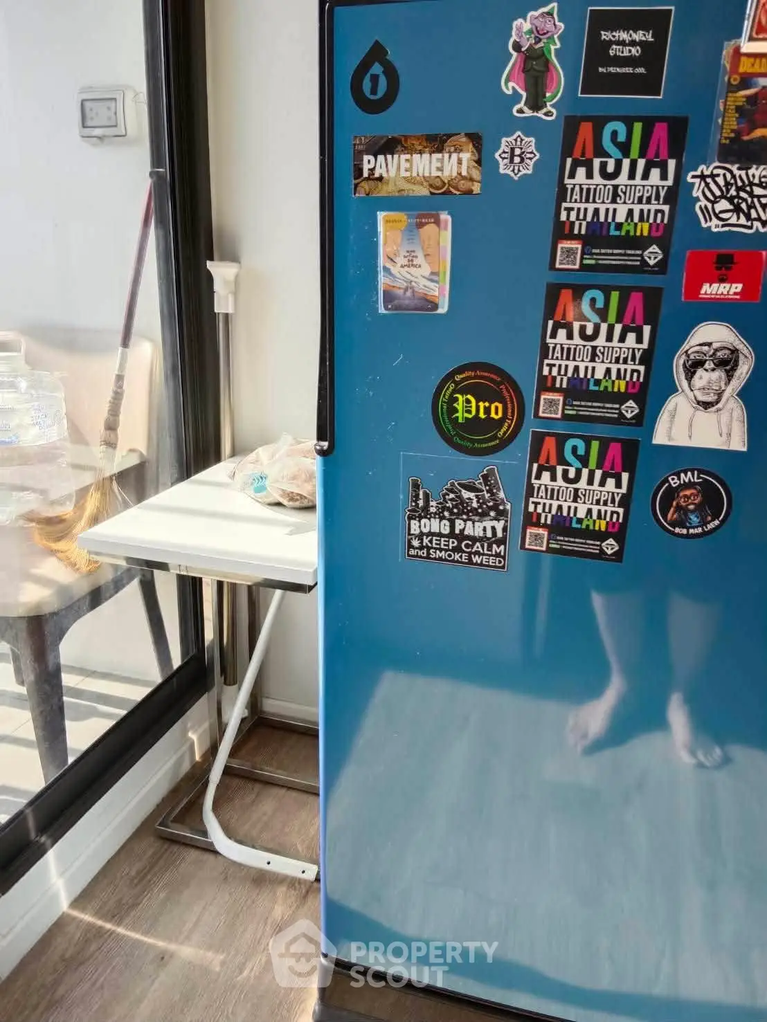 Modern kitchen with blue fridge adorned with vibrant stickers and a small dining table by the window.