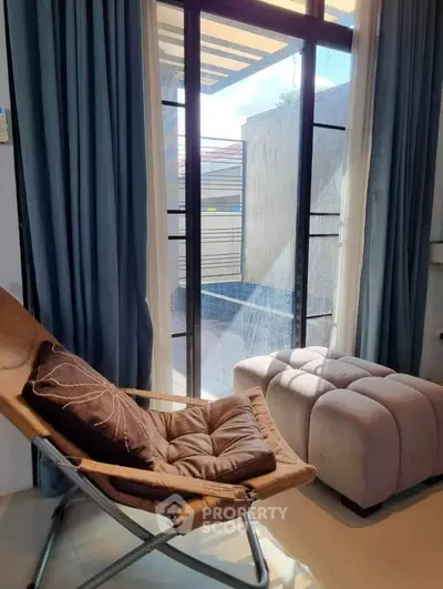 Cozy living room with stylish chair and ottoman by sunlit window, perfect for relaxation.