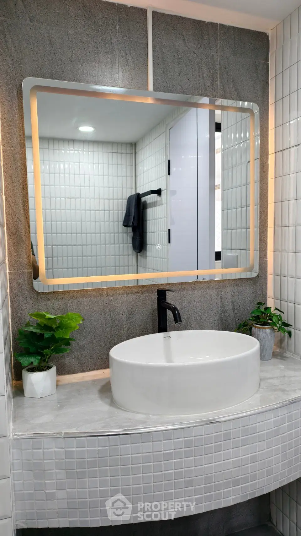 Modern bathroom with stylish round sink and illuminated mirror, featuring elegant tile design and potted plants.