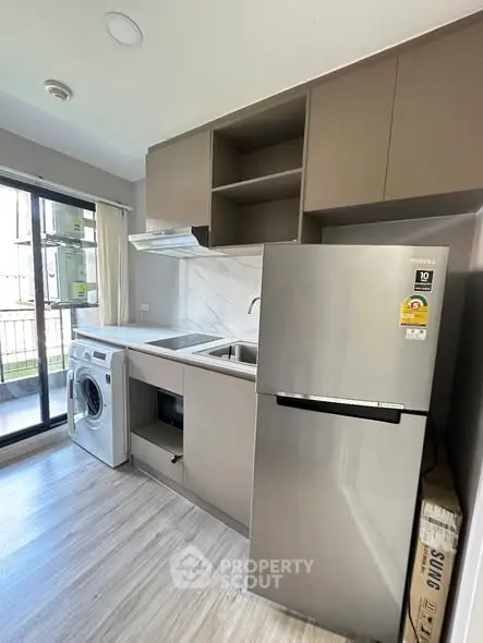 Modern kitchen with stainless steel fridge and washing machine, featuring sleek cabinetry and balcony access.