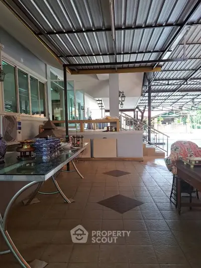 Spacious covered outdoor area with tiled flooring and glass tables, ideal for entertaining or relaxation.