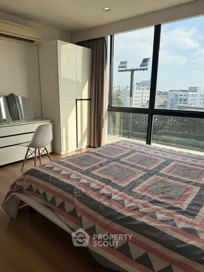 Bright bedroom with large windows and city view, featuring modern decor and ample natural light.