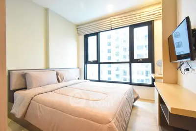 Modern bedroom with large window and city view, featuring a cozy bed and wall-mounted TV.