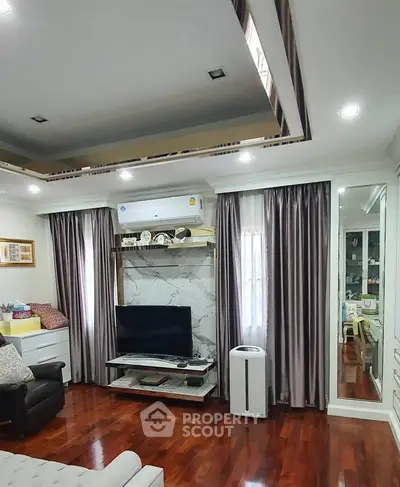 Elegant living room with hardwood floors, modern TV setup, and luxurious curtains.
