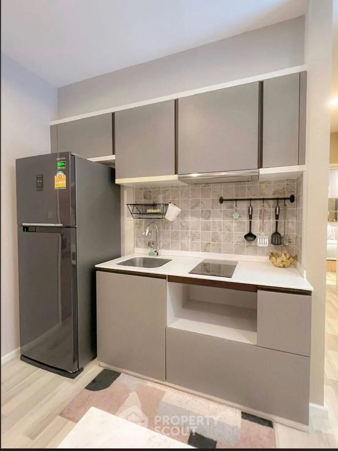 Modern compact kitchen with sleek cabinetry and stainless steel fridge in stylish apartment.