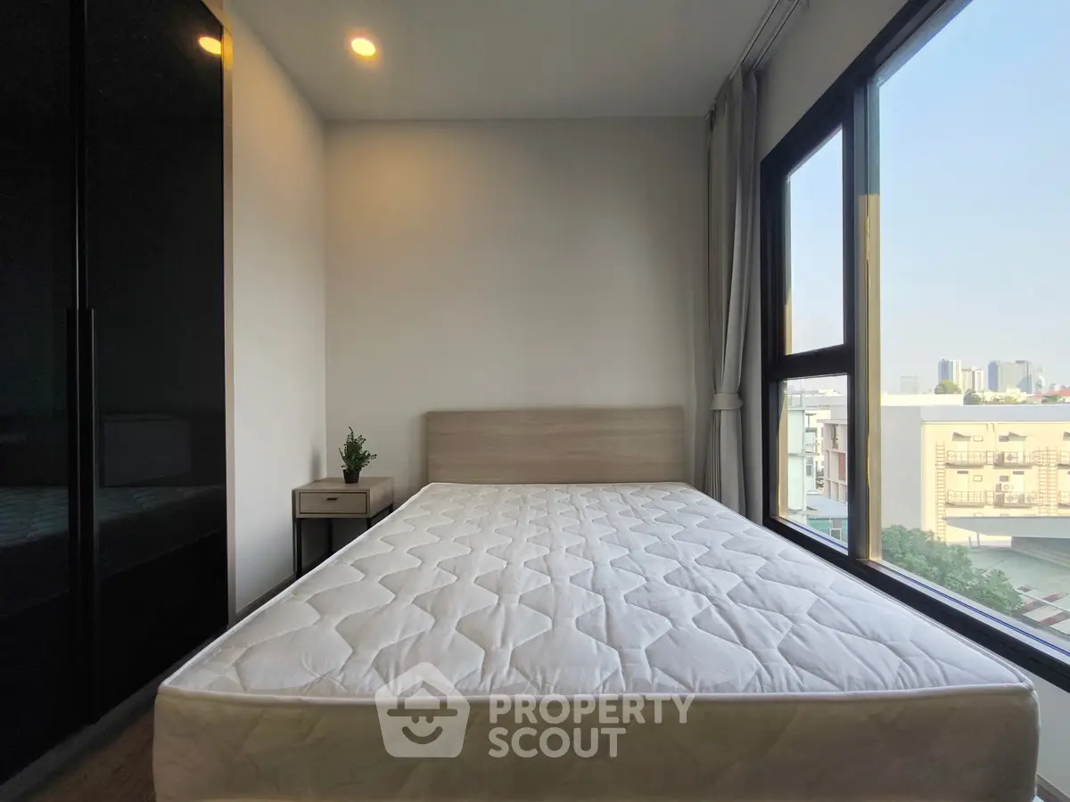 Modern bedroom with large window and city view, featuring a comfortable bed and sleek design.