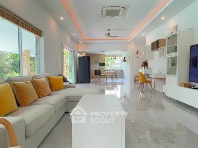 Spacious modern living room with open kitchen, featuring elegant decor and large windows for natural light.