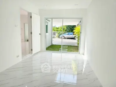Bright empty room with marble flooring and sliding glass doors leading to a small garden area.