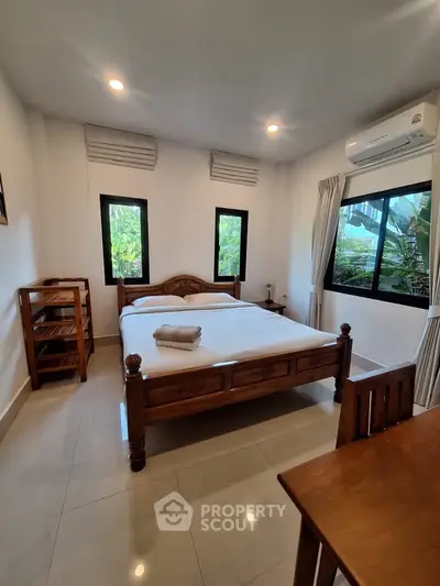 Cozy bedroom with wooden furniture and large windows offering garden views