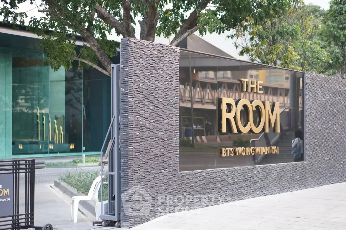 Modern building entrance with stylish signage and lush greenery.