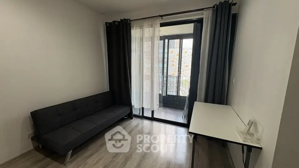 Modern living room with sleek black sofa and large window leading to balcony.
