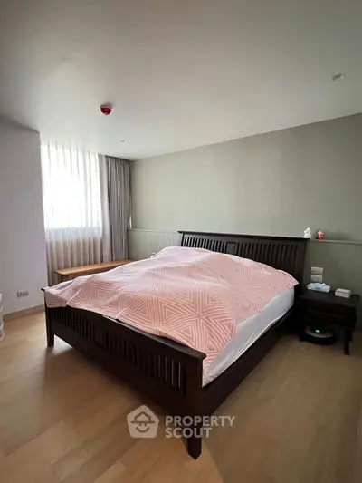 Spacious bedroom with modern wooden bed and natural light from large window.