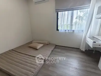 Minimalist bedroom with floor mattress and natural light through window.