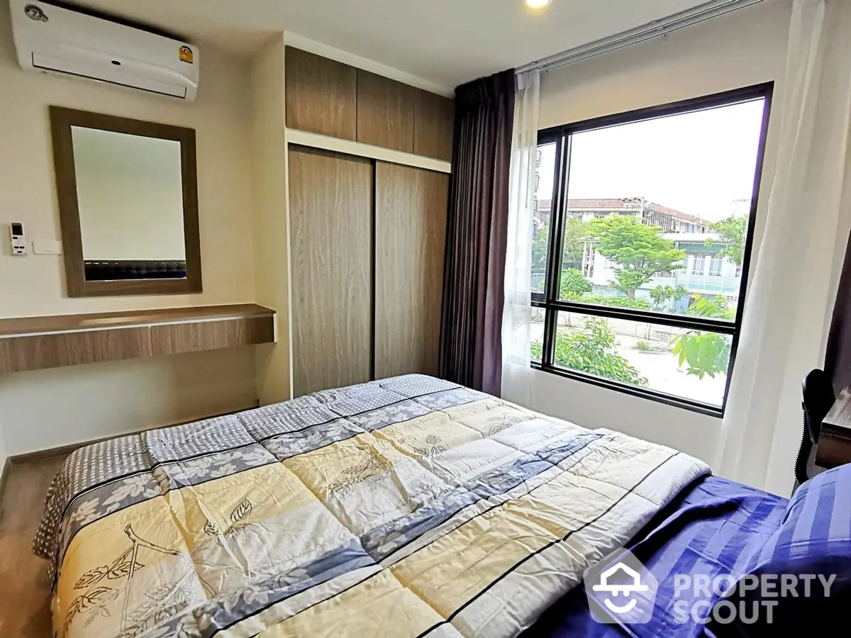 Cozy bedroom with large window offering natural light and a serene view, complemented by modern wooden furnishings and a comfortable bed.